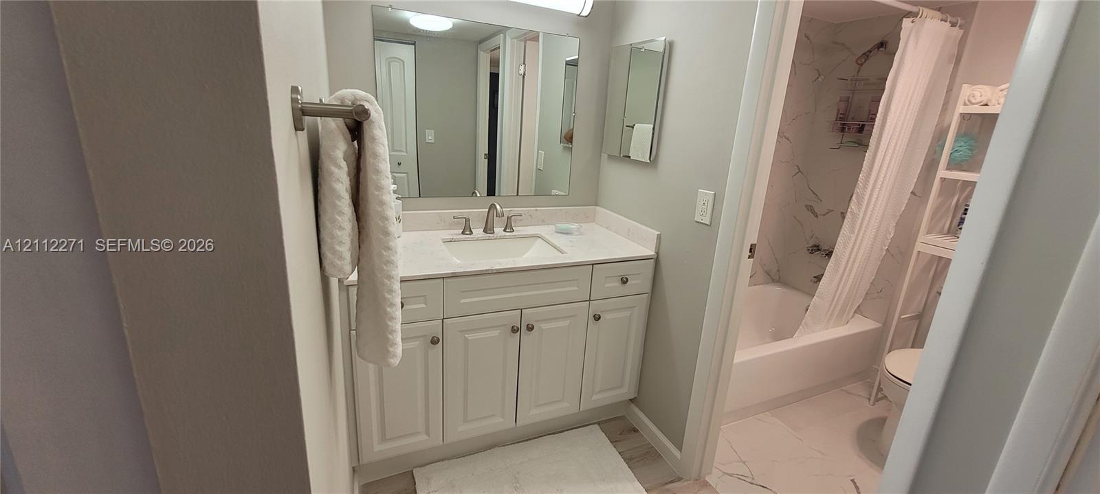 Bathroom featuring a vanity with shaker-style cabinetry, light-toned stone-finish countertop, integrated undermount sink, brushed nickel widespread faucet, and full-width vanity mirror