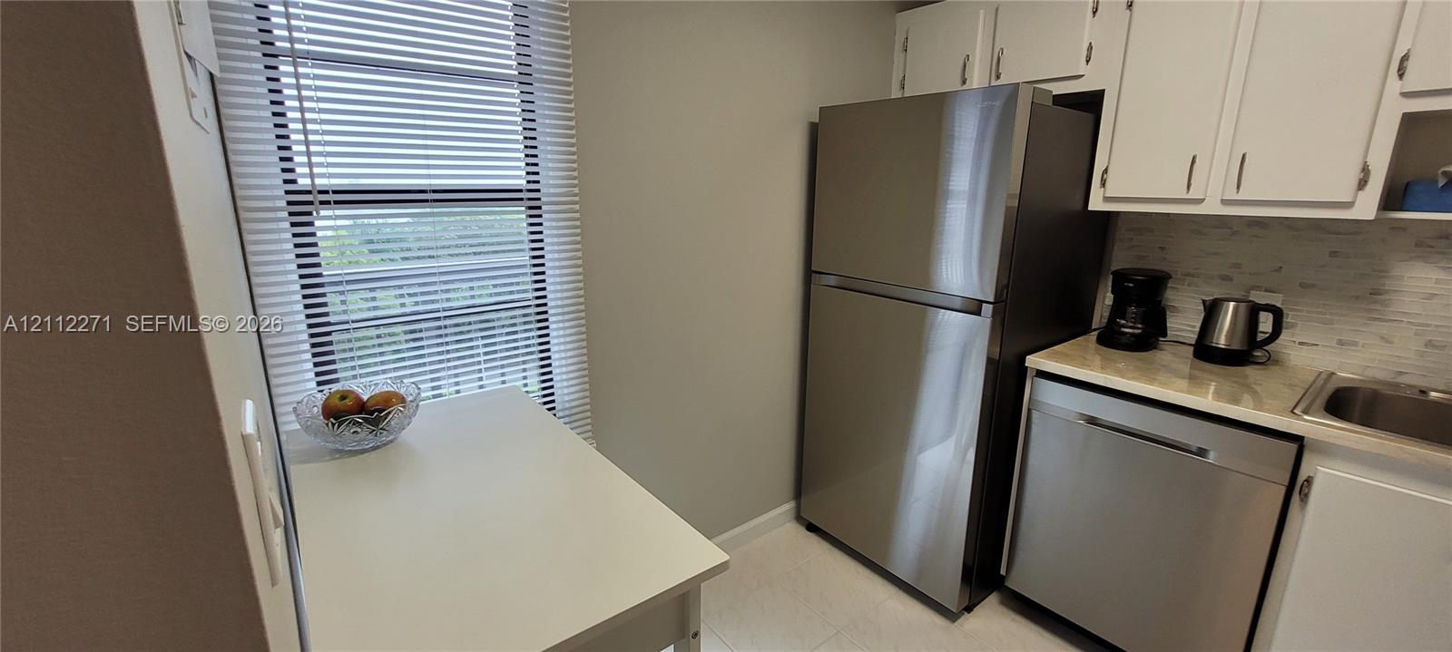 Kitchen featuring white cabinetry, stainless steel refrigerator and dishwasher, stone-finish countertop, and window with horizontal blinds