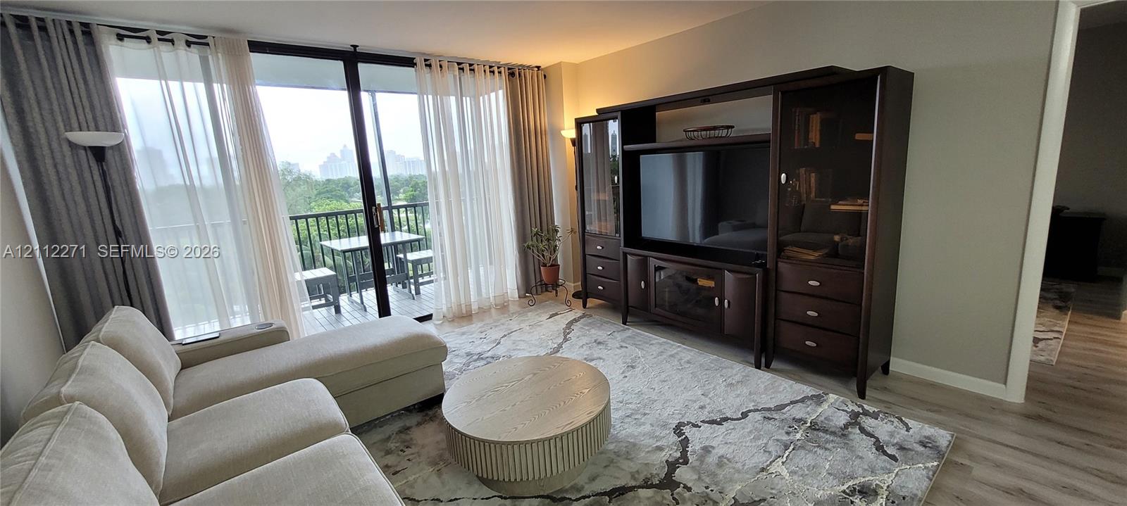 Floor-to-ceiling sliding glass doors providing outdoor access, balcony with metal railings, and light-tone wood-finish flooring
