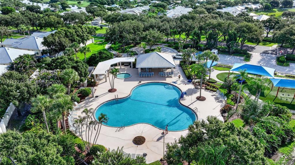 Community recreational area featuring a clover-shaped swimming pool, attached spa, covered pavilion, and shaded seating structures surrounded by landscaped grounds