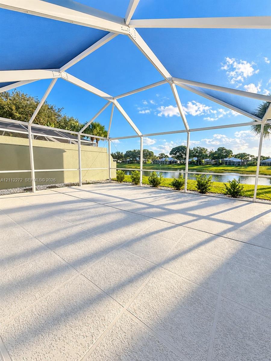 Screened lanai featuring a concrete patio, white metal framing, and water frontage with manicured landscaping