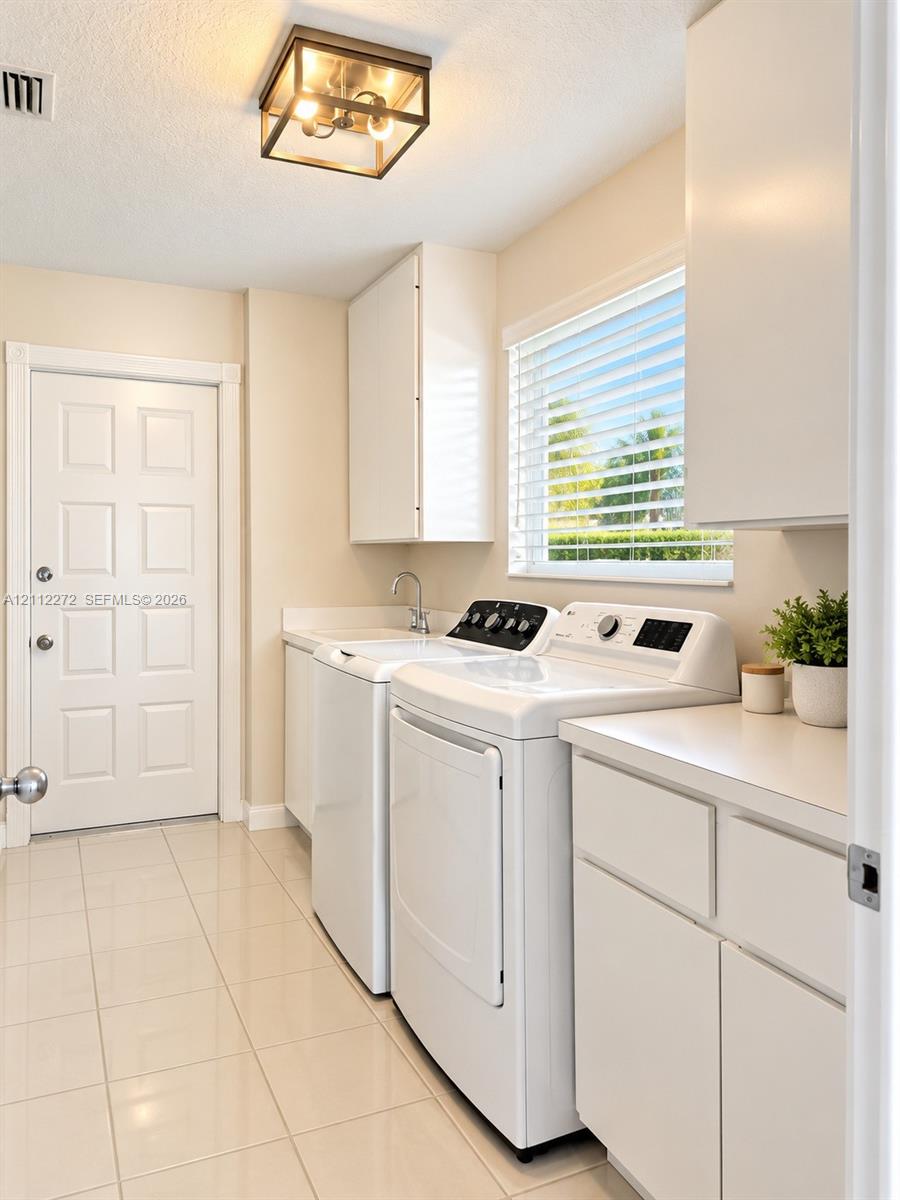 Laundry room featuring white cabinetry, solid-surface countertops, integrated utility sink with chrome faucet, ceramic tile flooring, and a flush-mount geometric ceiling light fixture
