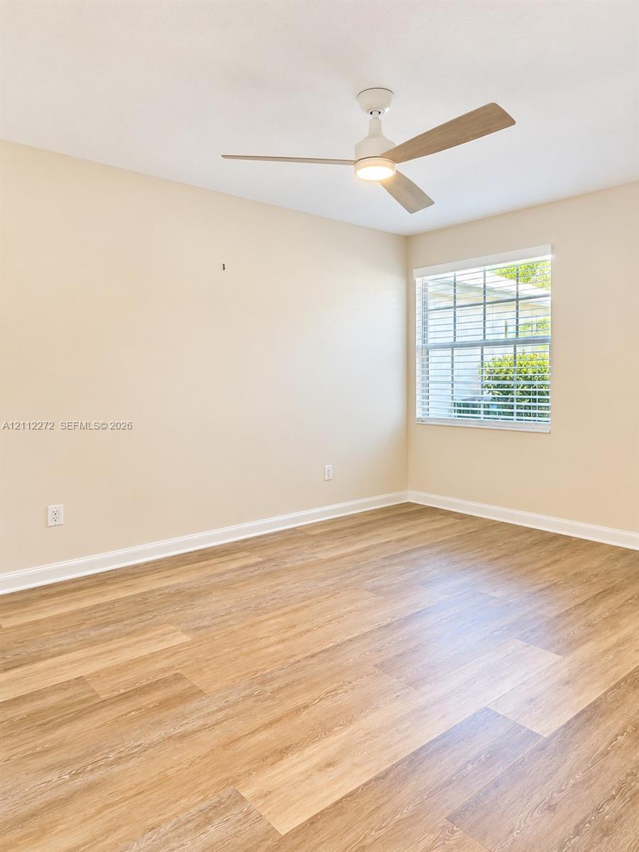 Neutral-toned interior featuring wood-finish flooring, a multi-blade ceiling fan with integrated lighting, and a single-pane window with grid inserts