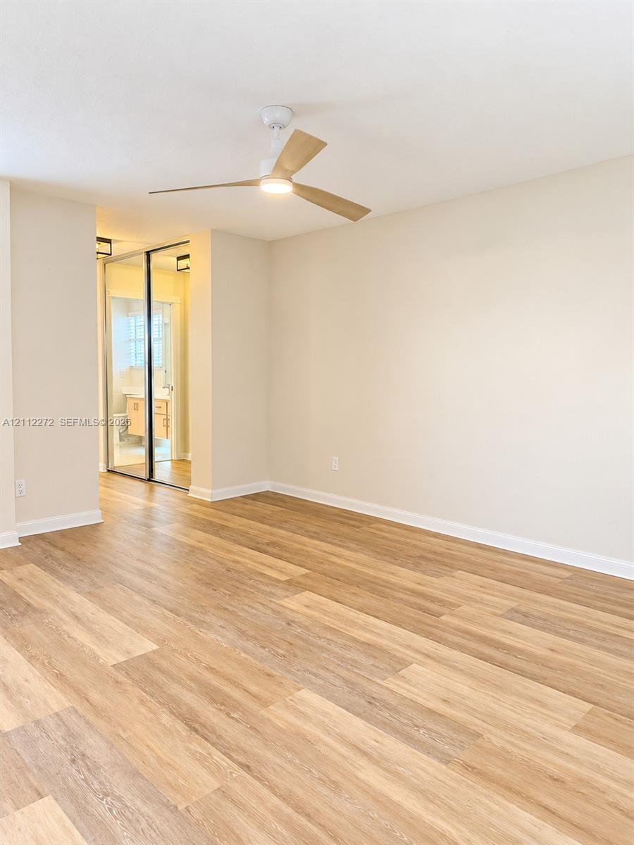 Interior space featuring wood-finish flooring, a contemporary three-blade ceiling fan with integrated lighting, and mirrored closet doors