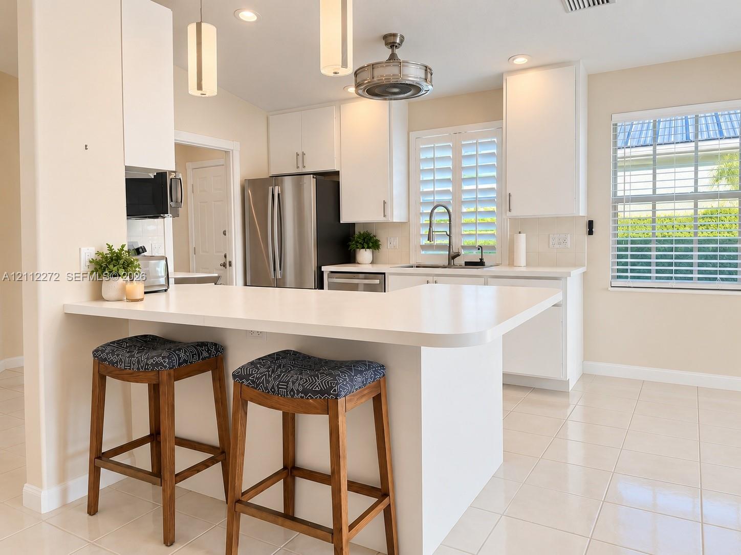 Kitchen featuring white cabinetry, solid-surface countertops with an integrated breakfast bar, stainless steel appliances, tile flooring, and interior window shutters