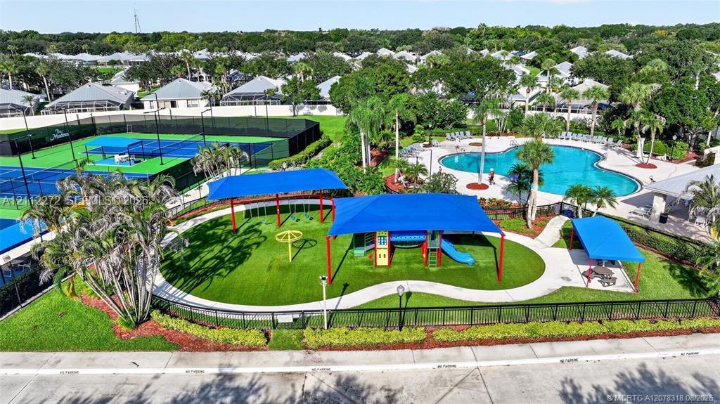 Recreational facility featuring a swimming pool, fenced tennis courts, and a shaded playground area with synthetic turf