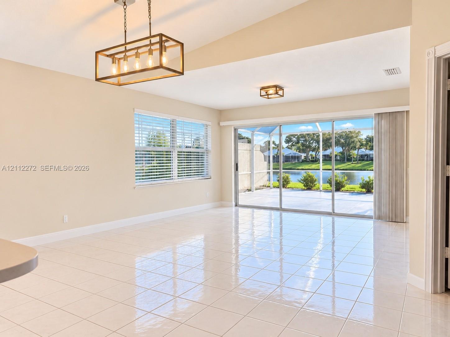 Vaulted ceilings, large-format tile flooring, rectangular lantern-style pendant lighting, and oversized sliding glass doors opening to a screened patio