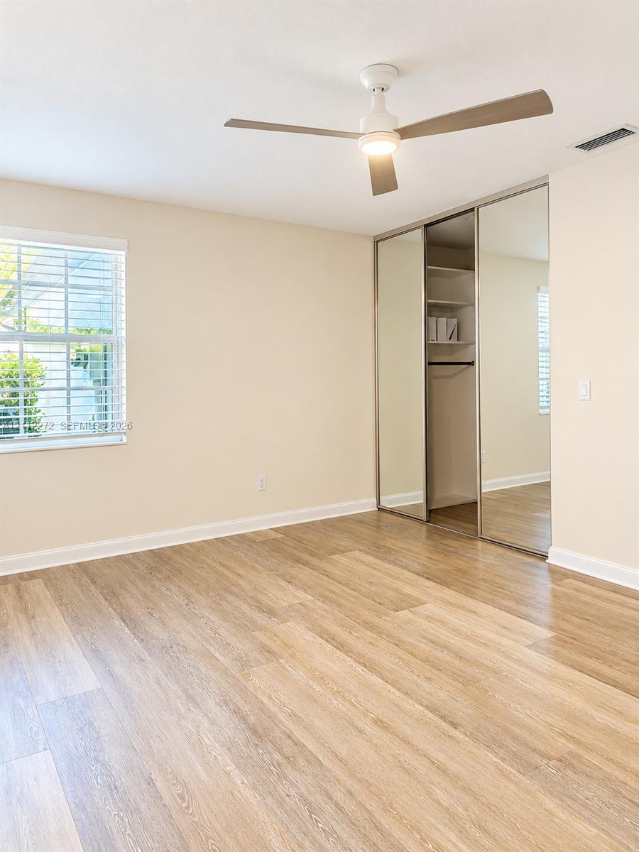 Wood-finish flooring, ceiling fan with integrated lighting, and dual-panel sliding mirror closet with built-in shelving