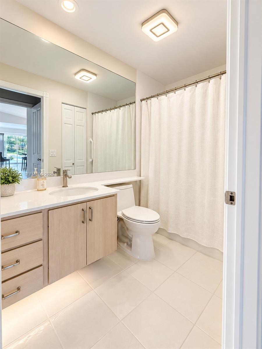 Floating vanity with light wood-finish cabinetry, solid surface countertop, integrated sink, full-width vanity mirror, and square recessed lighting fixtures
