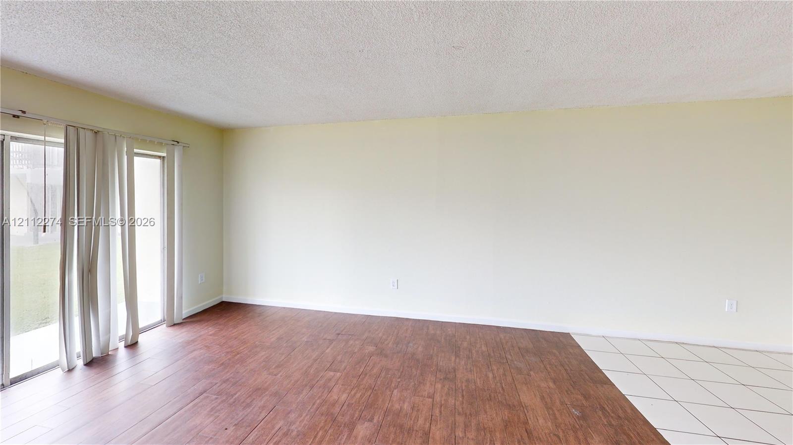 Interior room featuring wood-finish flooring, white tile flooring, and large sliding glass doors Interior room featuring wood-finish flooring, white tile flooring, and large sliding glass doors