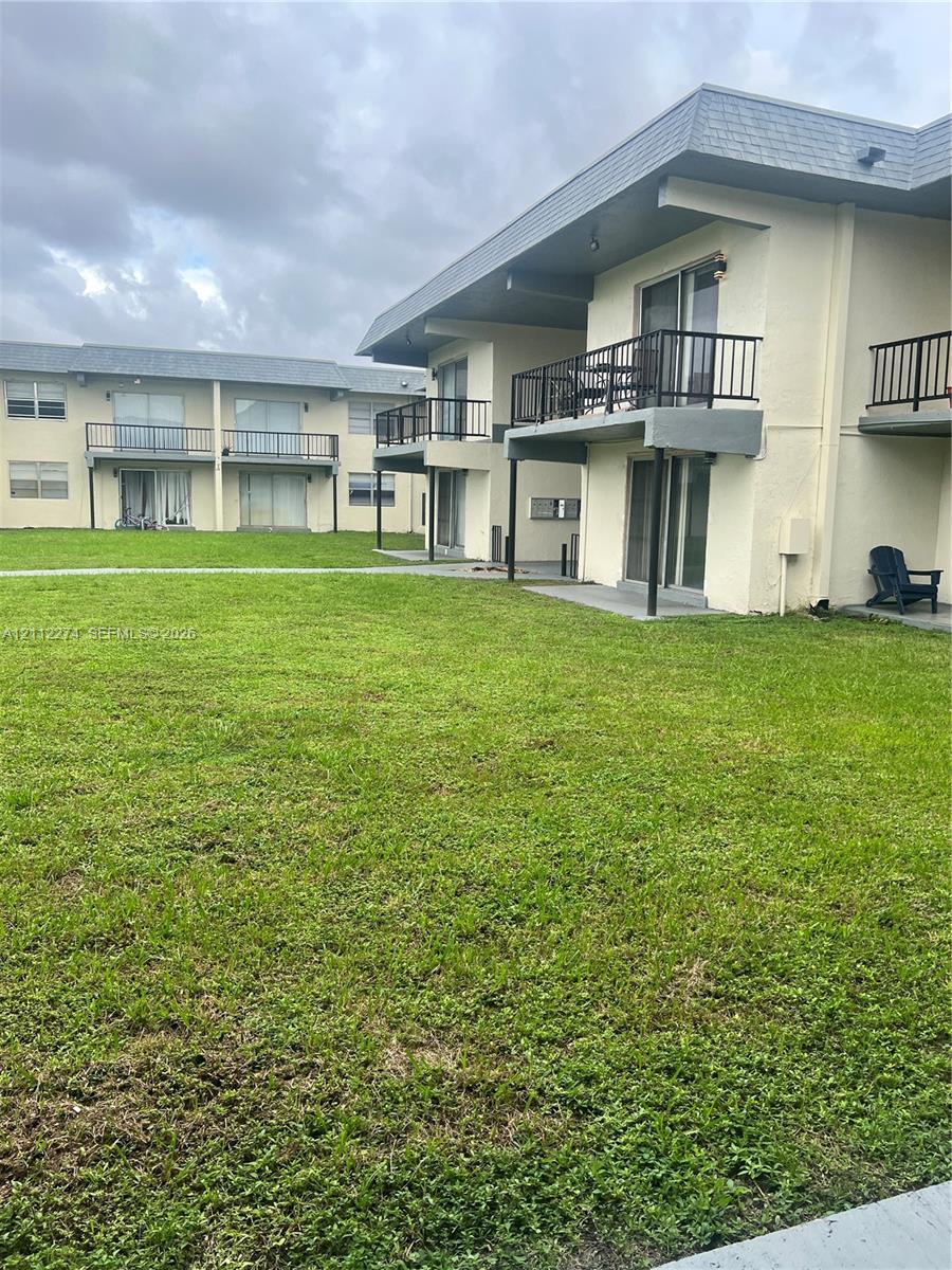 Exterior facade featuring stucco siding, elevated balconies with metal railings, sliding glass doors, and expansive grassy grounds Exterior facade featuring stucco siding, elevated balconies with metal railings, sliding glass doors, and expansive grassy grounds