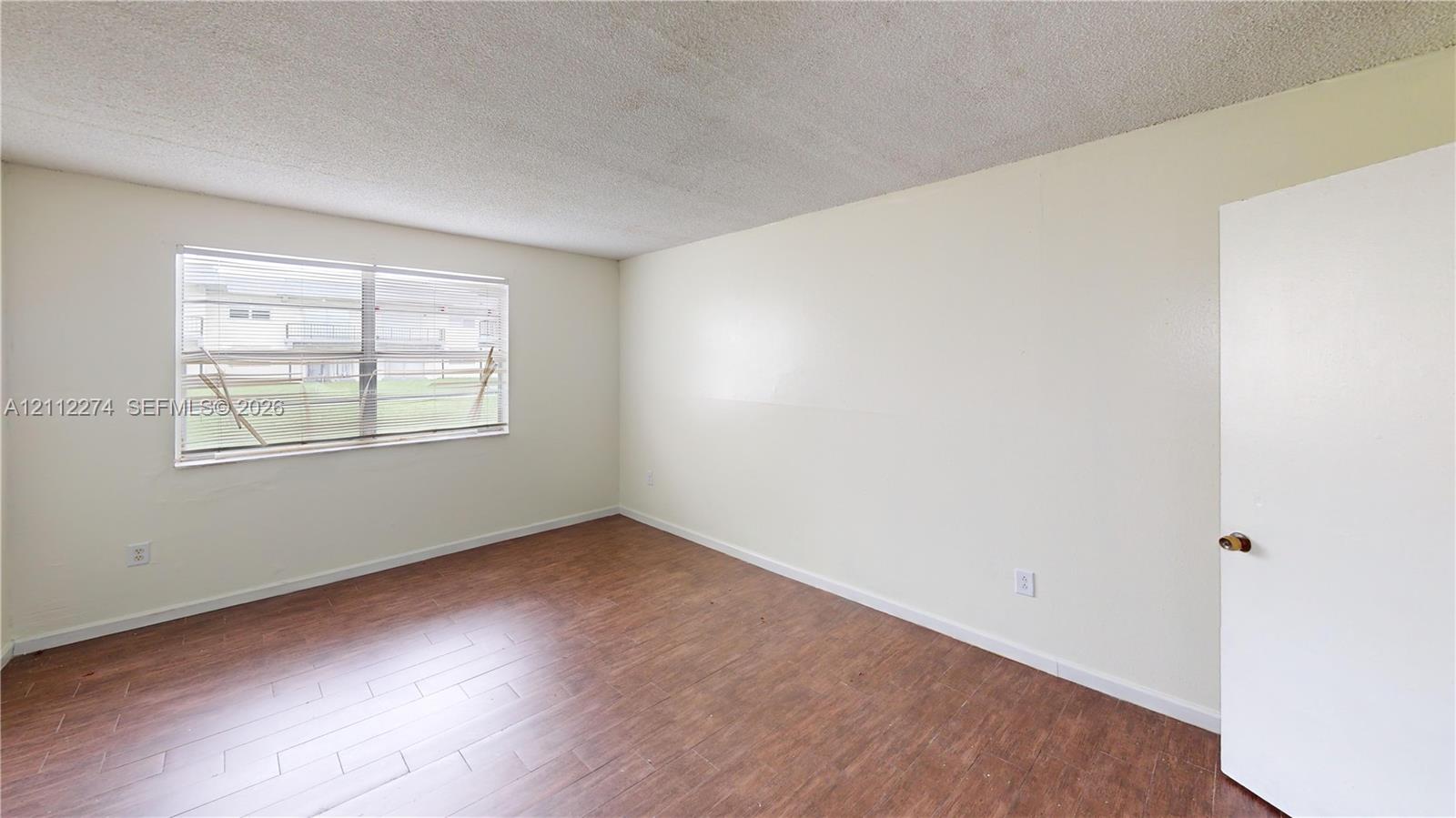Room interior featuring wood-finish flooring, neutral wall paint, and a single-pane horizontal window Room interior featuring wood-finish flooring, neutral wall paint, and a single-pane horizontal window