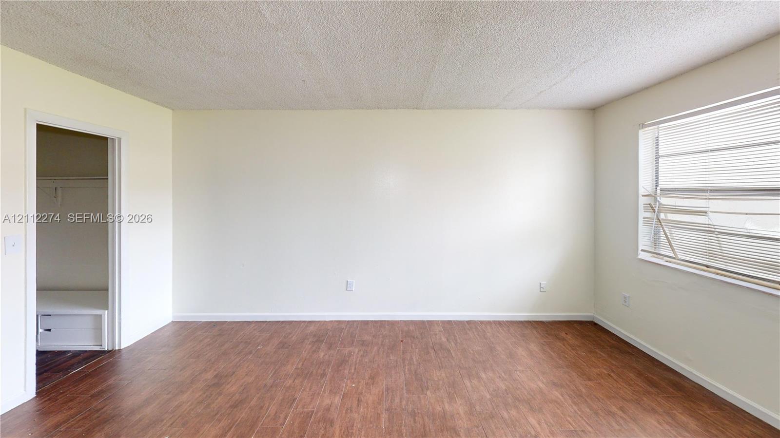 Neutral-toned interior space featuring wood-finish flooring, textured ceiling, and a closet with built-in shelving Neutral-toned interior space featuring wood-finish flooring, textured ceiling, and a closet with built-in shelving