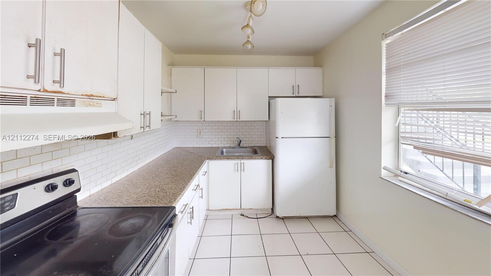 Kitchen featuring white cabinetry, solid surface countertops, a white tile backsplash, ceramic tile flooring, and integrated white appliances Kitchen featuring white cabinetry, solid surface countertops, a white tile backsplash, ceramic tile flooring, and integrated white appliances