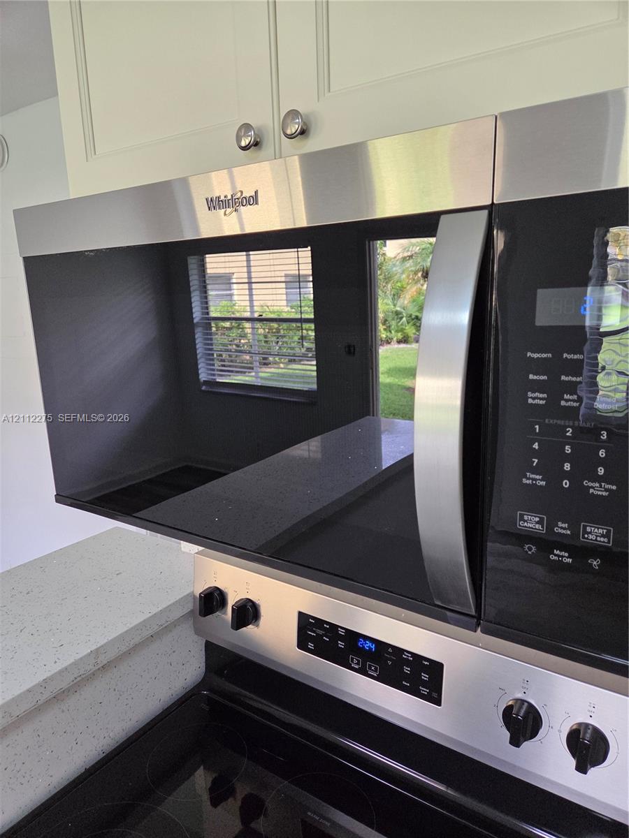 Stainless steel over-the-range microwave, smooth-top electric range, light-toned shaker-style cabinetry, and quartz countertops with integrated fleck detailing