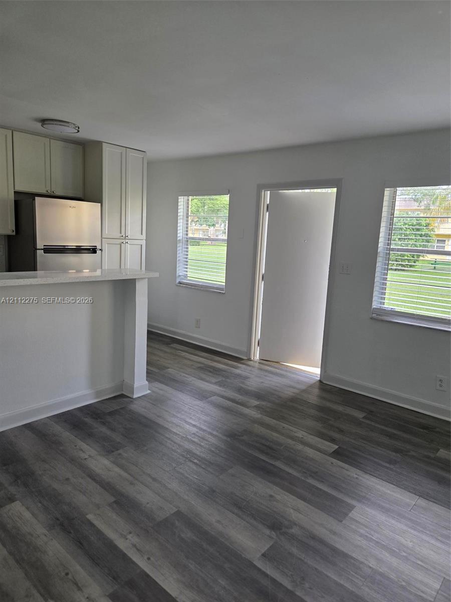 Kitchen featuring light-toned cabinetry, stainless steel appliances, a peninsula breakfast bar with light-toned countertop, and wood-finish flooring throughout
