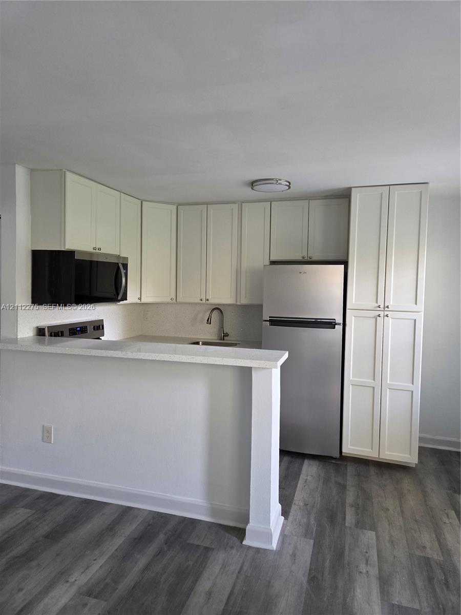 Kitchen featuring white shaker-style cabinetry, a stone-finish countertop with an integrated breakfast bar, stainless steel appliances, and wood-finish flooring