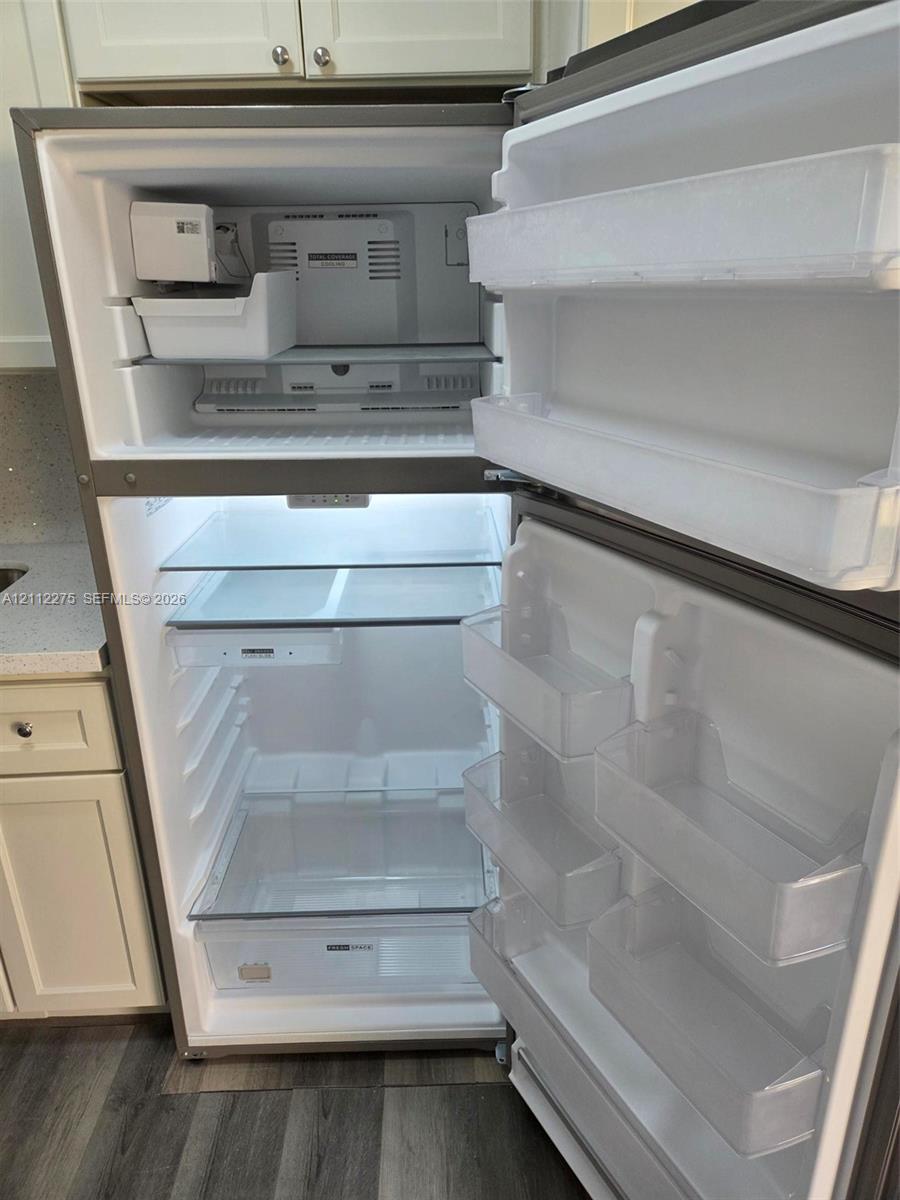 Stainless steel top-freezer refrigerator featuring an integrated ice maker, adjustable glass shelving, clear produce drawers, and interior LED lighting