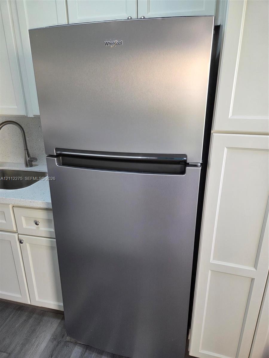 Stainless steel top-freezer refrigerator, white shaker-style cabinetry, solid-surface countertop, and stainless steel sink with a high-arch faucet
