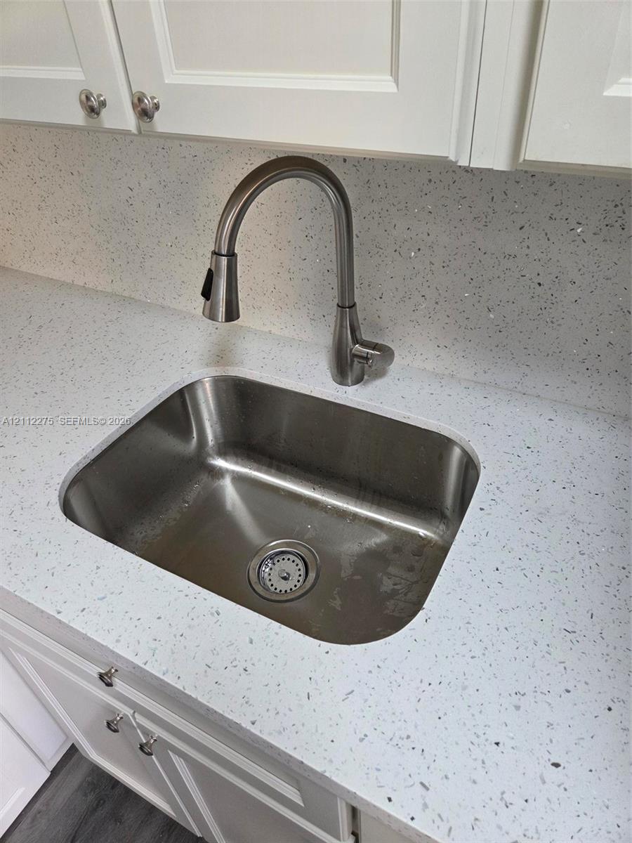 Stainless steel undermount sink featuring a high-arc pull-down faucet, white solid-surface countertop with integrated backsplash, and shaker-style cabinetry