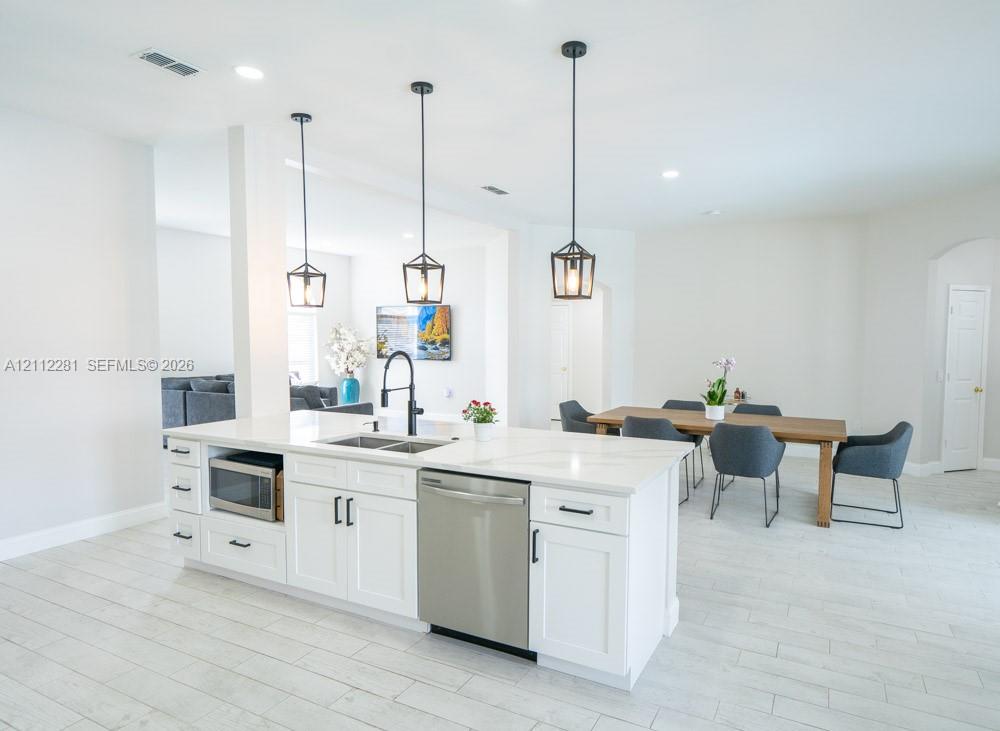 Kitchen island featuring white shaker-style cabinetry, quartz countertops, a stainless steel dishwasher, an undermount sink with a matte black faucet, and three pendant lights