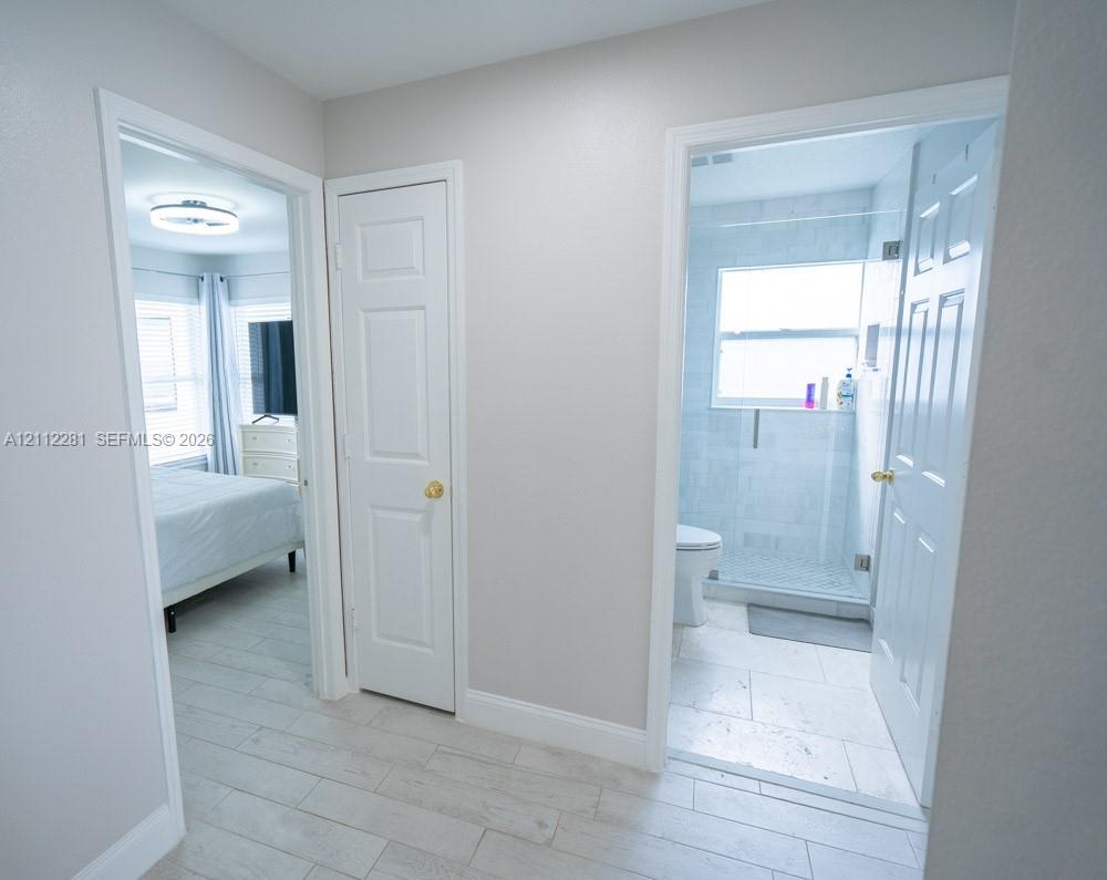 Hallway featuring wood-finish flooring, white panel doors, and entry into a bathroom with tile surround shower