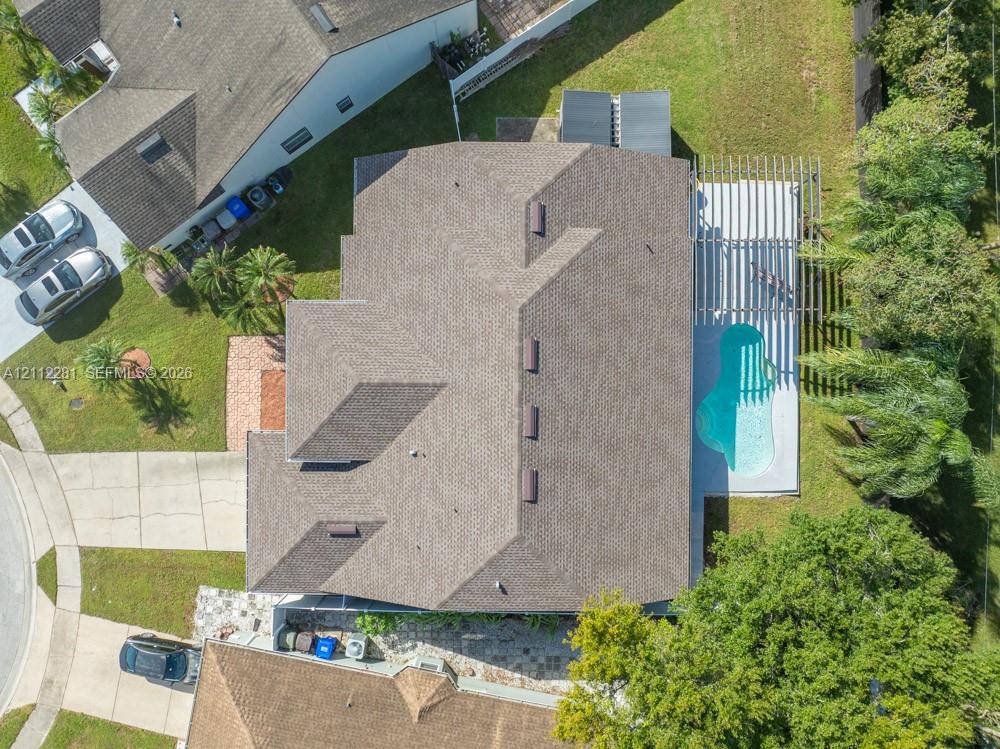 Aerial view of property featuring a shingled roof, a backyard swimming pool, a patio pergola, and mature landscaping