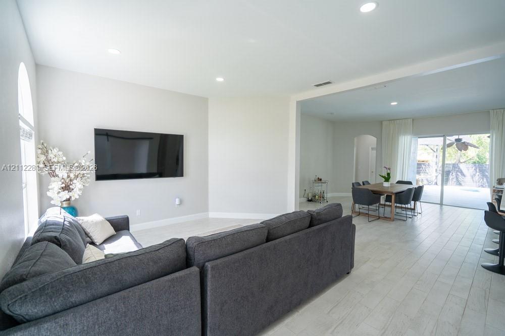 Open-concept interior featuring light-toned tile flooring, recessed ceiling lighting, arched wall detailing, and glass sliding doors