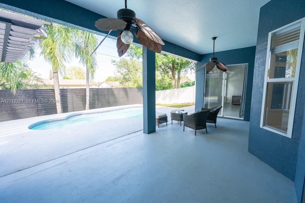 Covered patio featuring two ceiling fans, painted exterior wall finish, and direct access to an in-ground swimming pool enclosed by privacy fencing