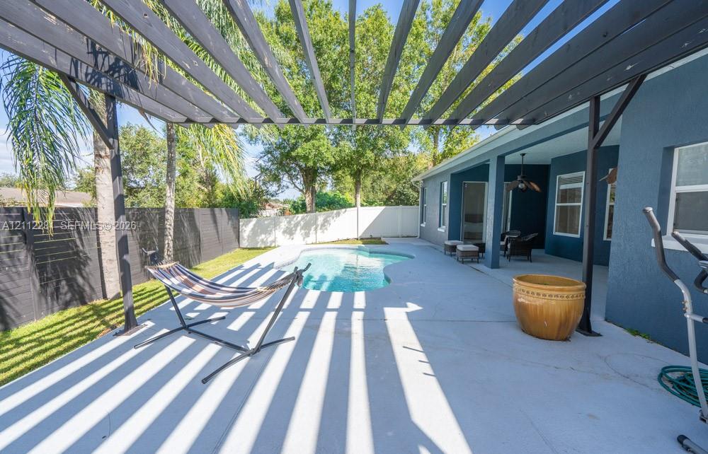 Covered patio with a custom wood-beam pergola, swimming pool, concrete hardscaping, and perimeter fencing