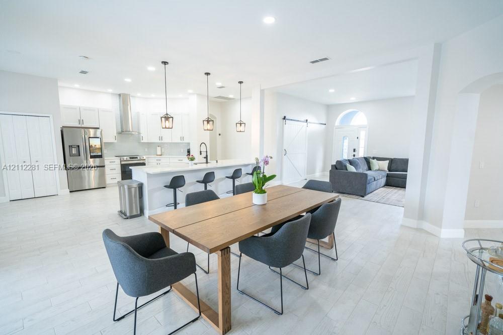 Open-concept kitchen featuring shaker-style cabinetry, quartz countertops, a stainless steel chimney-style range hood, pendant lighting, and wood-finish tile flooring