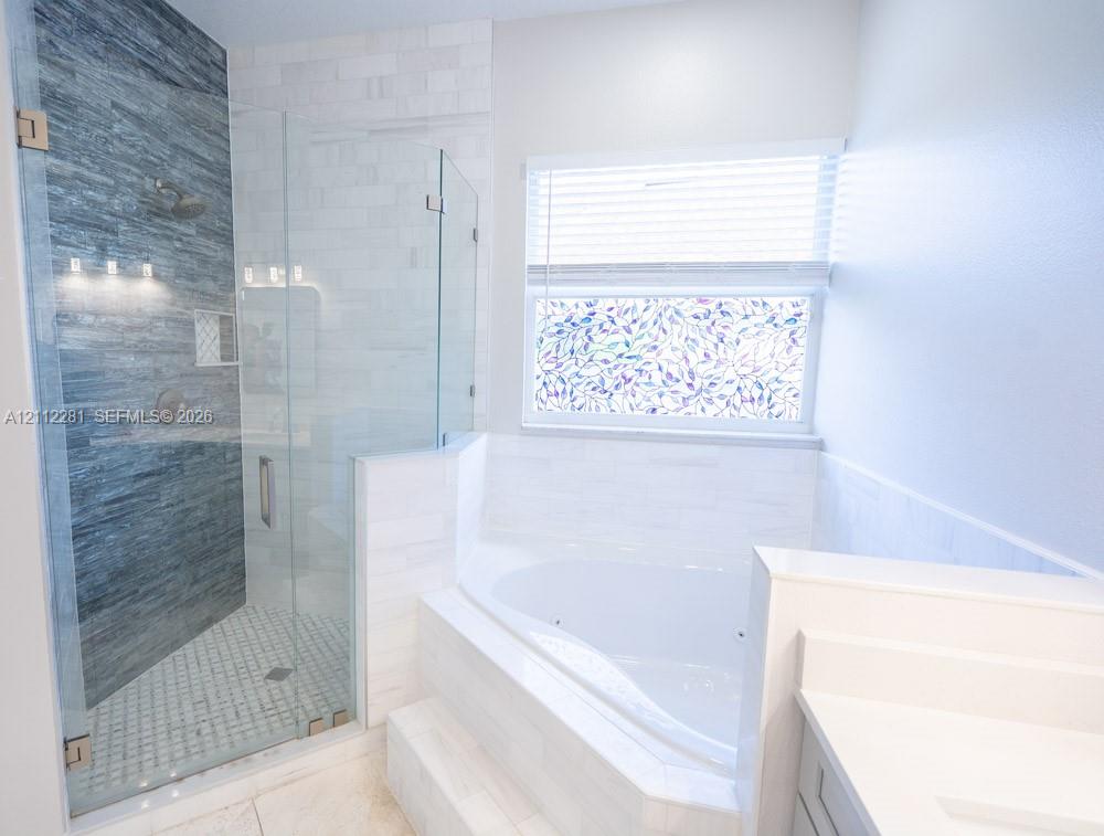 Walk-in glass-enclosed shower with horizontal textured tiling and built-in shelving, alongside a white jetted soaking tub with tile surround