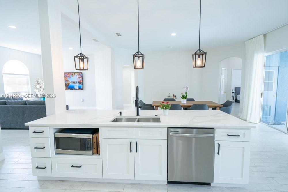 Kitchen island featuring stone-look countertops, white shaker-style cabinetry, matte black hardware, three geometric pendant lights, and a stainless steel undermount sink with a high-arch faucet
