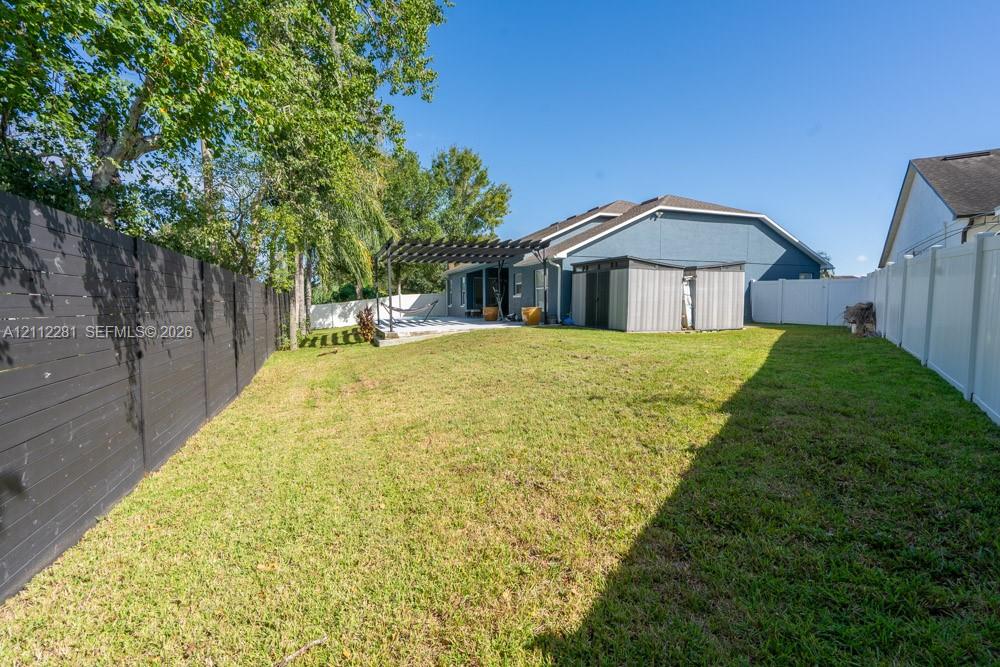 Fenced backyard featuring a manicured lawn, wooden pergola, and mature trees