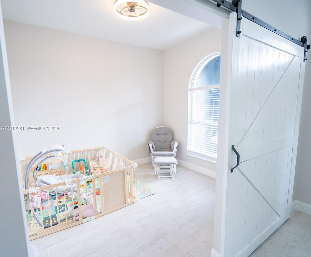 Flexible office/den featuring a white sliding barn door, arched window, wood-finish flooring, and a modern flush-mount ceiling light