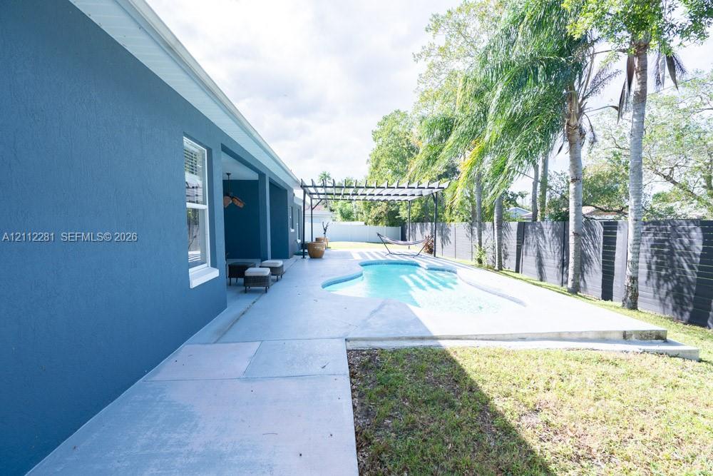 Private backyard featuring a swimming pool, concrete patio, wooden pergola, and perimeter fencing