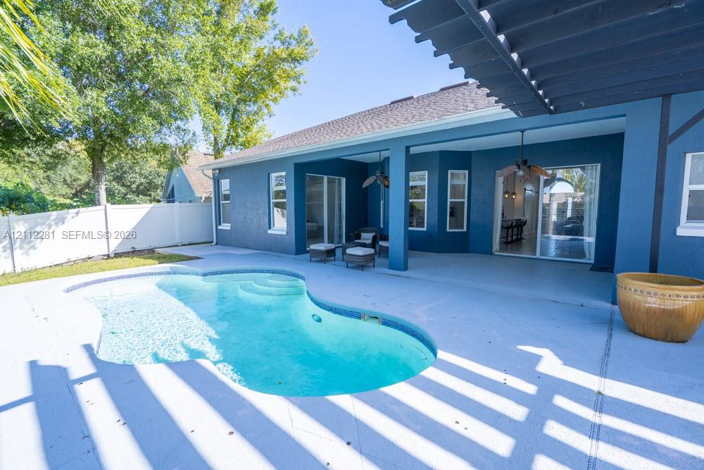 Covered rear patio featuring a pergola, concrete decking, and an inground swimming pool with integrated steps, enclosed by privacy fencing