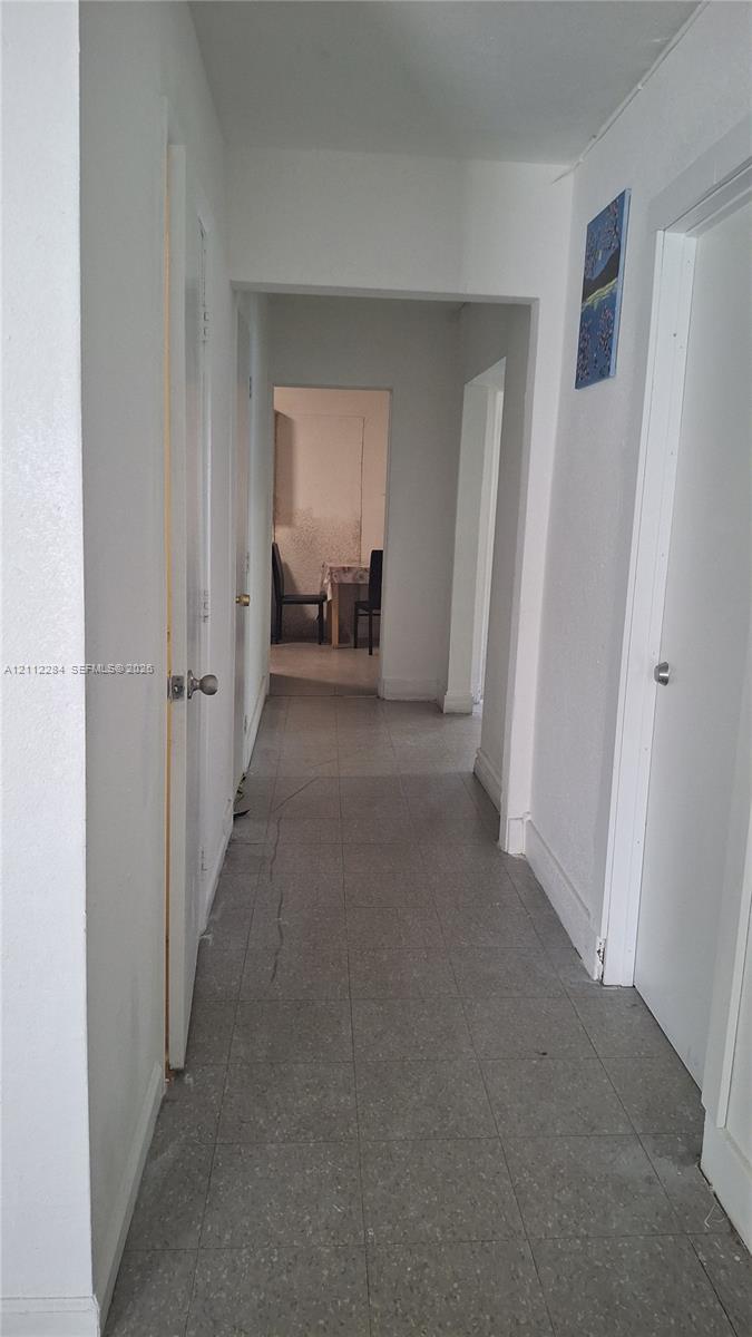 Interior hallway featuring neutral walls, white doors, and grey tile flooring