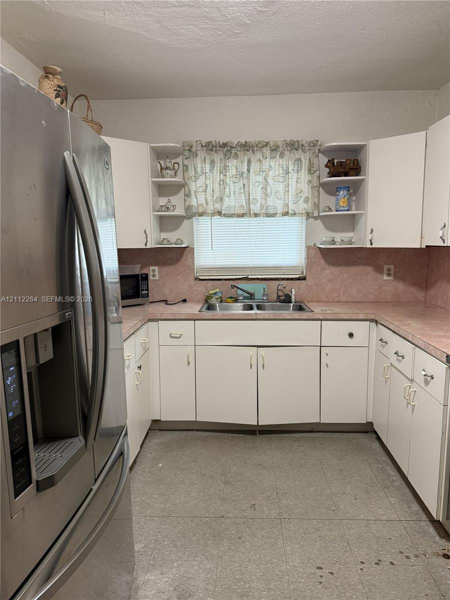 Kitchen featuring white cabinetry with open shelving, stainless steel refrigerator, solid-surface countertops, and dual-basin stainless steel sink
