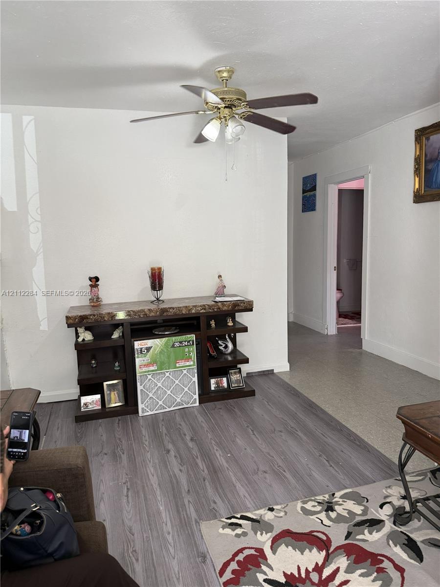 Interior space featuring grey wood-finish flooring and a multi-blade ceiling fan with an integrated three-light fixture