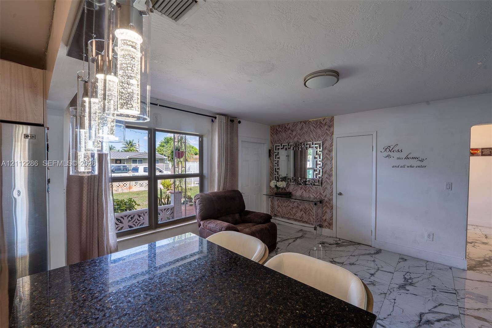 Open-concept living space featuring high-gloss marbled flooring, a stone-surfaced kitchen island, three-pendant glass cylinder light fixtures, and a decorative textured accent wall