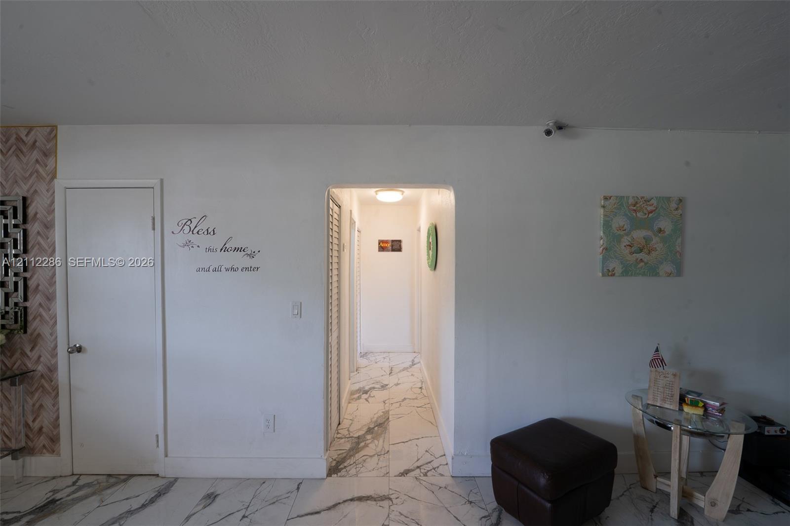 Interior space featuring white-veined stone-finish flooring, an arched entryway, louvered-door closet, and overhead flush-mount lighting