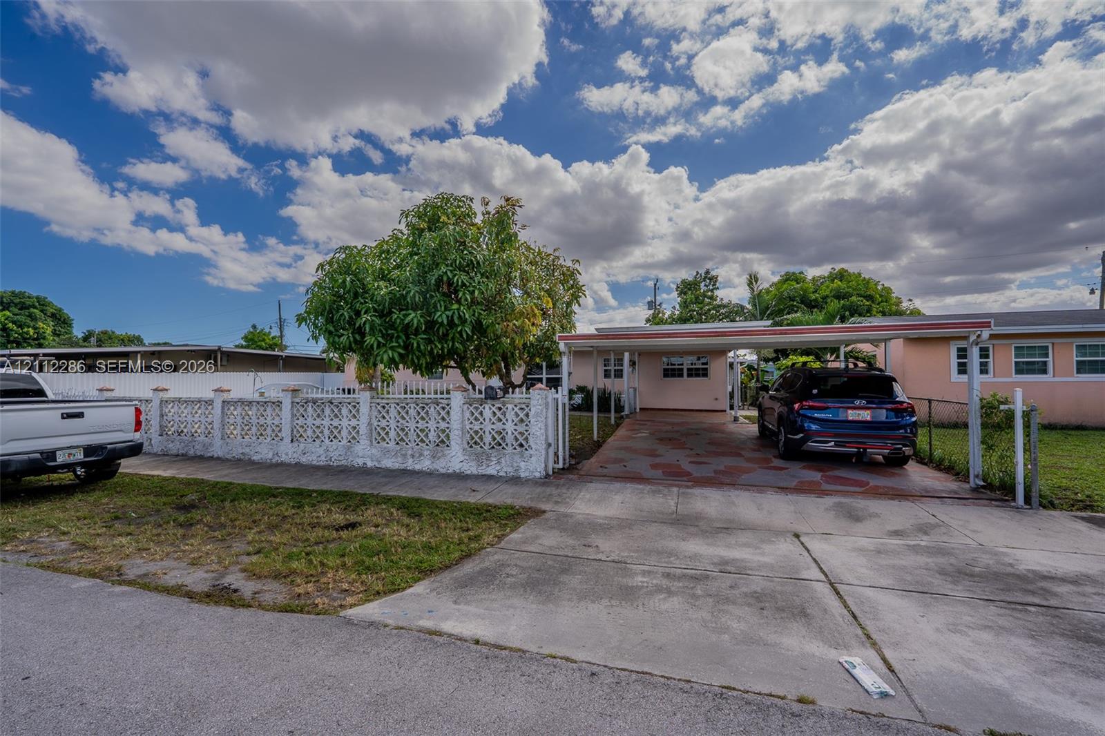 Exterior featuring a covered carport, decorative breeze block fencing, paved driveway, and mature landscaping