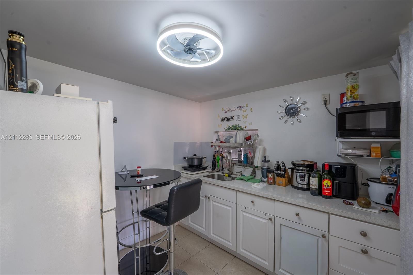 White cabinetry, integrated stainless steel sink, solid-surface countertop, and circular LED ceiling fixture