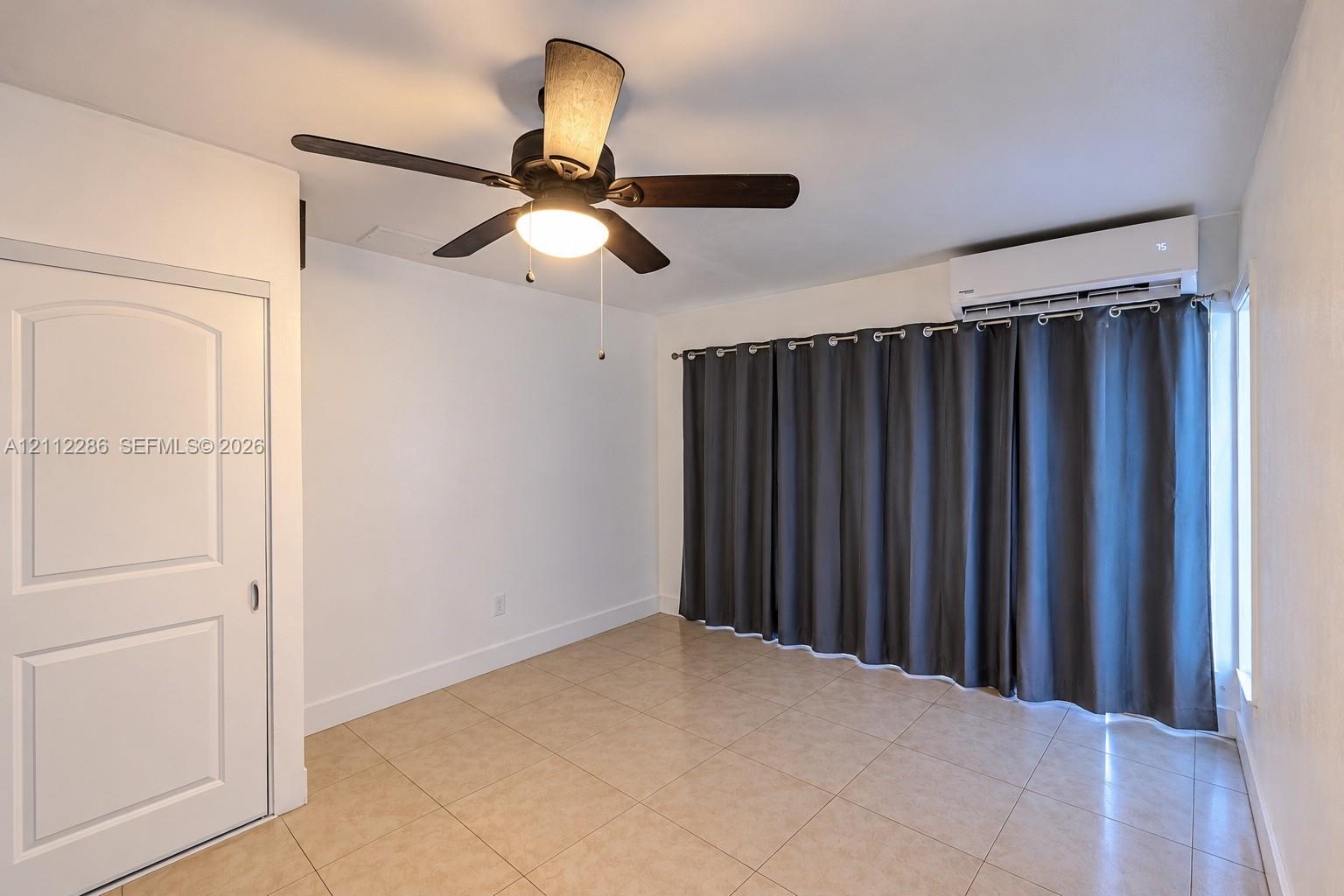 Interior space featuring neutral tile flooring, a wall-mounted ductless mini-split air conditioning unit, and a ceiling fan with integrated lighting