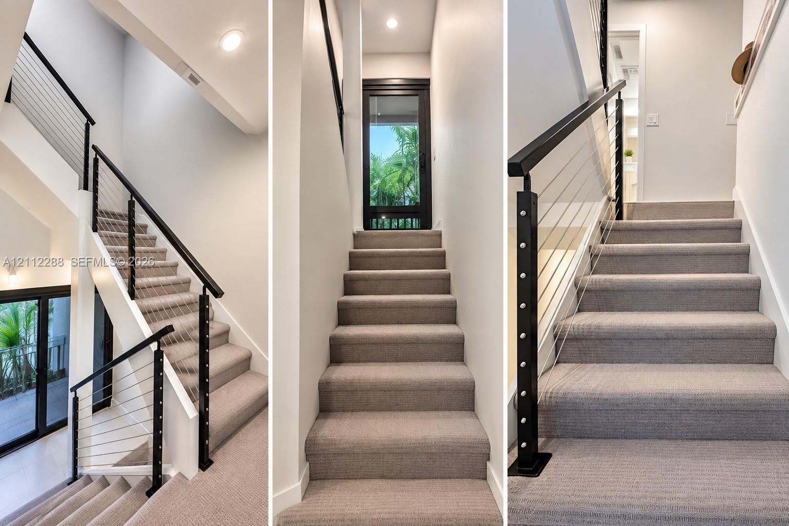 Staircase featuring neutral carpeted treads, a black metal handrail, horizontal cable railing system, and recessed ceiling lighting
