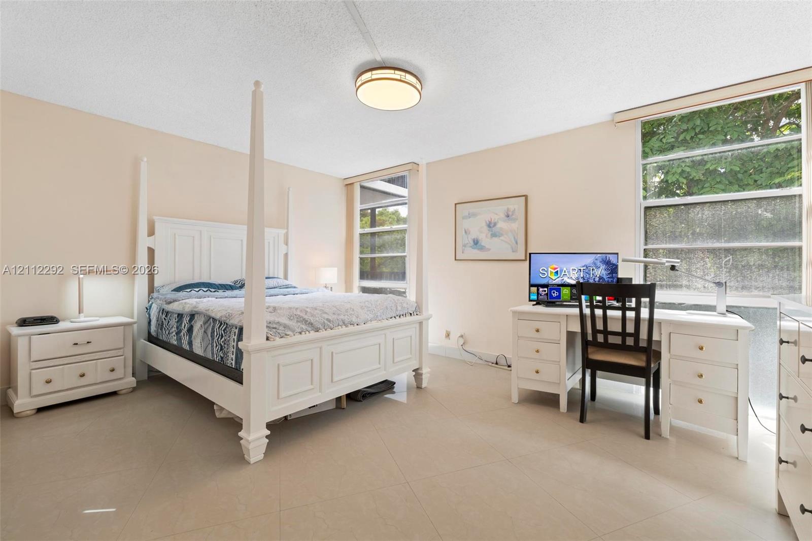 Neutral-toned tile flooring, large windows with natural lighting, and a circular flush-mount ceiling fixture