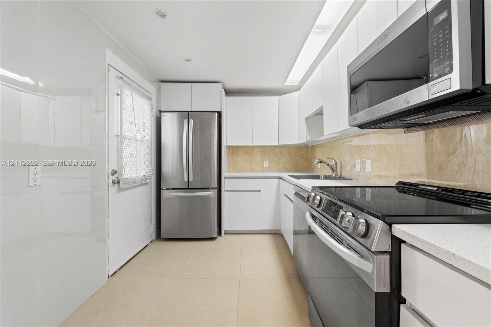 Kitchen featuring white cabinetry, light-toned stone tile backsplash, stainless steel appliances, and tile flooring