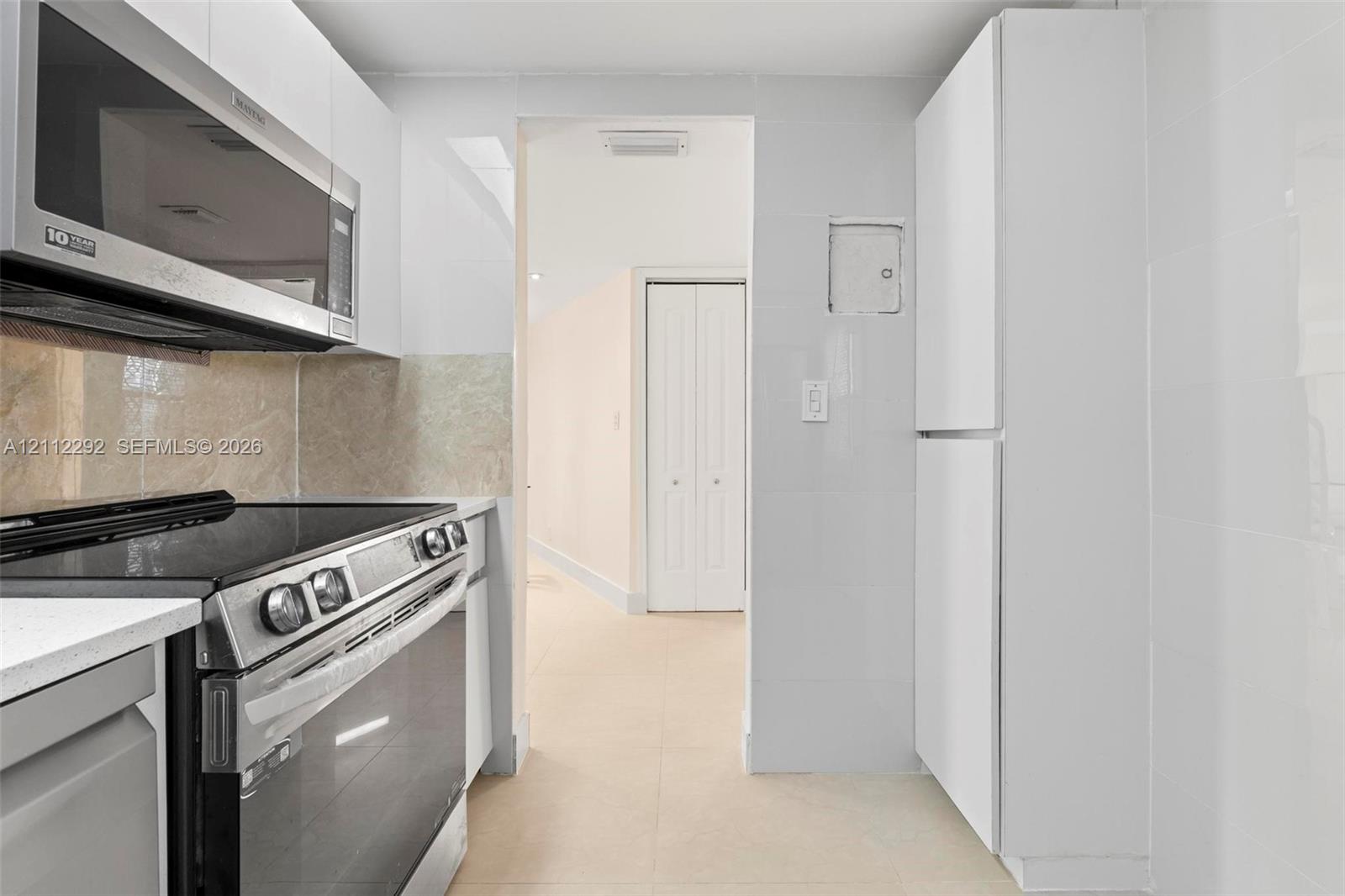 Kitchen featuring white flat-panel cabinetry, stainless steel appliance suite, tiled backsplash, and light-toned flooring