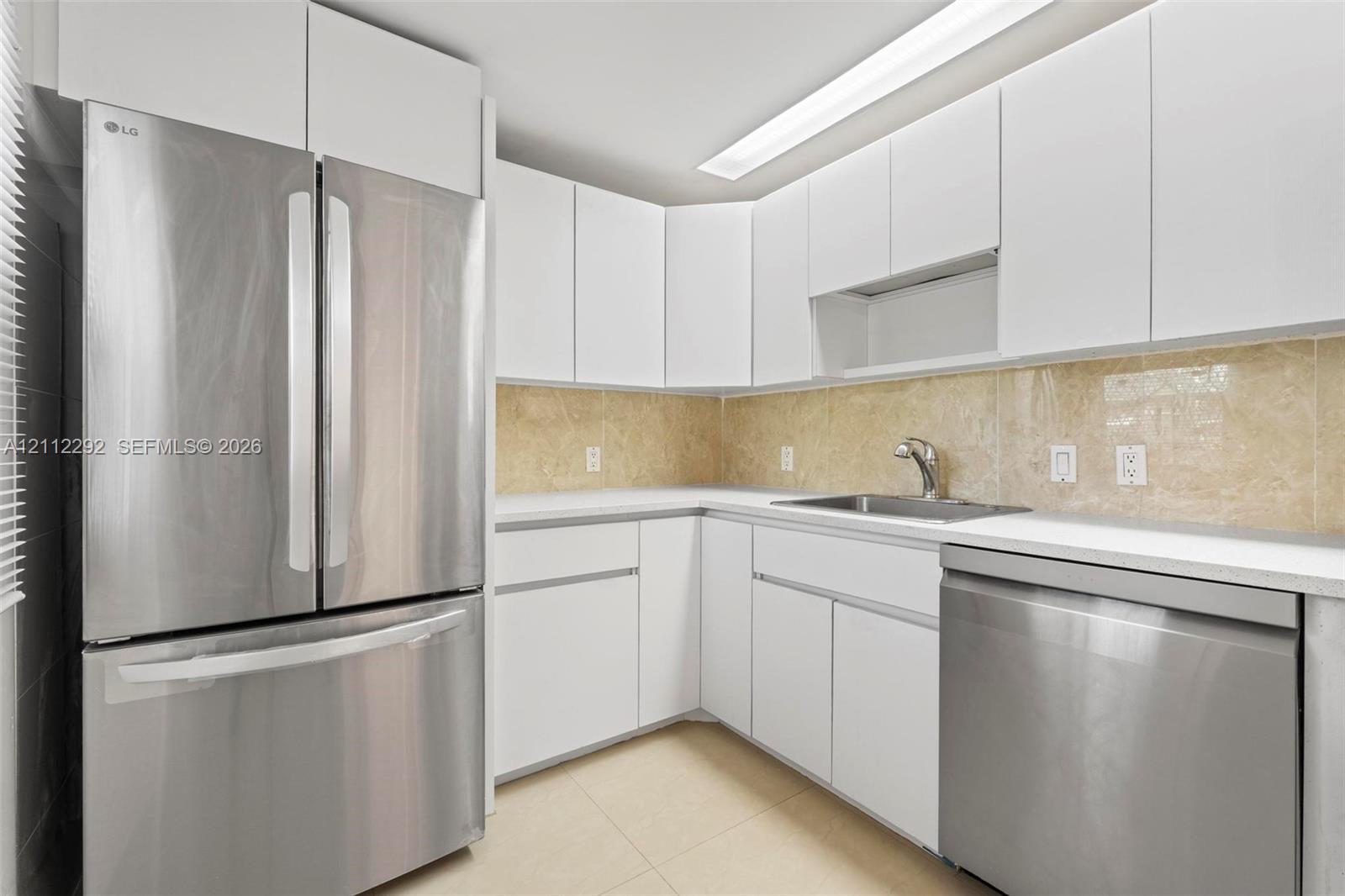 Kitchen featuring flat-panel white cabinetry, stainless steel appliances, neutral stone-finish backsplash, and an undermount sink with a gooseneck faucet